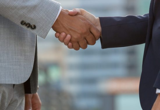 Businesspeople standing in city street and shaking hands. Business man and woman in office suits meeting outside. Successful partnership concept